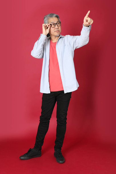 The senior Asian man wearing blue shirt with long hair standing on the red background. - Fotó, kép
