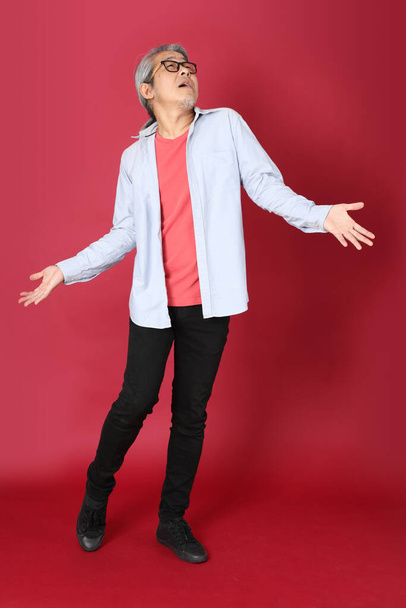 The senior Asian man wearing blue shirt with long hair standing on the red background. - Photo, image