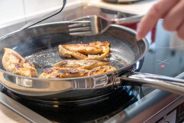 Woman cooking and frying chicken breasts and chicken filet in a pan on an hot stove in the kitchen as delicious meal and diet dinner cuisine for healthy nutrition with smoking hot meat and barbecue - Photo, Image