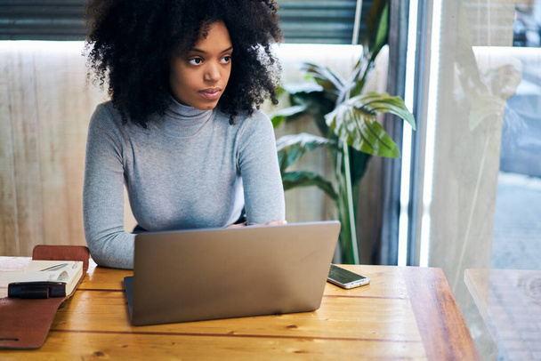 From above of pensive African American female freelancer in casual outfit looking away while working on remote project on laptop - Фото, зображення