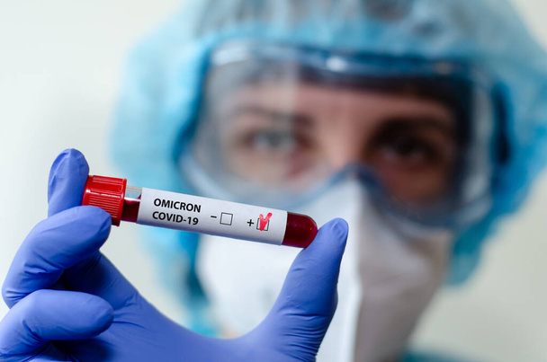 Assistant de laboratoire médical tenant une éprouvette avec un échantillon de sang test positif Omicron COVID-19. - Photo, image