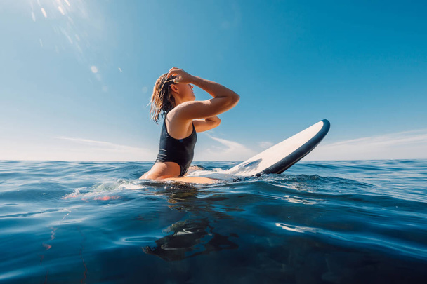 Zonnige dag met aantrekkelijke surf meisje wachtgolven op surfplank in de oceaan. - Foto, afbeelding