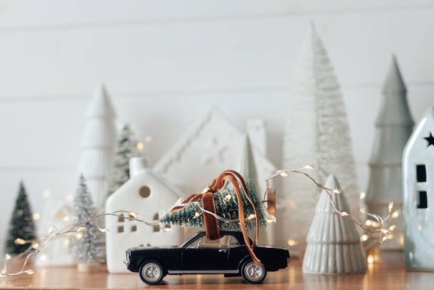 Holidays coming! Festive Christmas scene, miniature holiday village. Car with christmas tree, little houses and snowy trees on white background. Merry Christmas and Happy New Year ! - Photo, Image