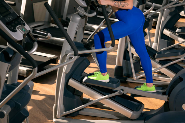 タイトなレギンスの女性の足は楕円形のトレーナーに従事している。ジムでの心臓トレーニング - 写真・画像