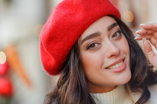 Kerst straat stijl portret van jonge mooie vrouw in rode baret wandelen in de Europese stad voor de wintervakantie. Stijlvol model met krullend haar doet nieuwjaarsboodschappen. Gezellig. - Foto, afbeelding