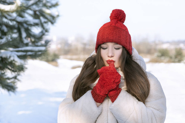 Joven mujer hermosa en rojo sombrero de punto y mitones calienta sus manos en invierno al aire libre. Caperucita roja. - Foto, Imagen