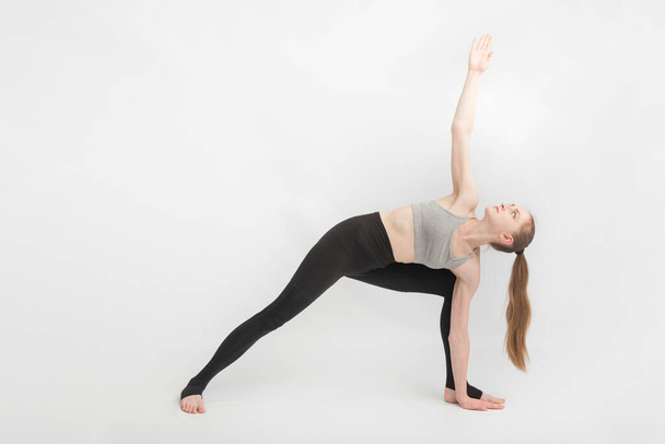 Triangle Pose. Trikonasana. Sports girl does yoga and performs asanas on white background. Gymnastics, stretching - Photo, image