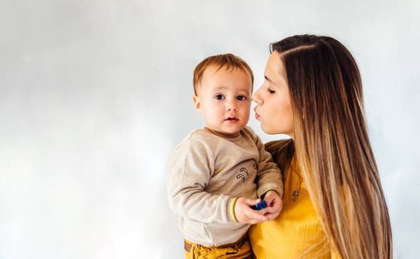 Portrait of young business mother woman kissing her baby boy in white background. Mum and son concept. - Foto, Bild