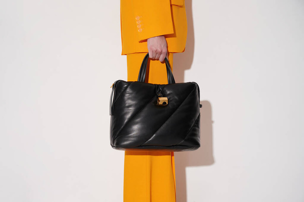 Woman in an orange suit with black leather handbag in her hand on the white background. Quilted tote bag stylish accessory. New collection or sale background. Horizontal photo with copy space. - Photo, Image