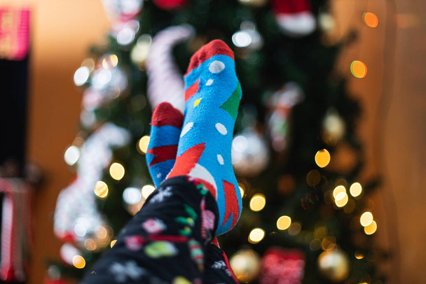 A closeup shot of a person holding up their feet in pajamas and socks near a Christmas tree - Zdjęcie, obraz