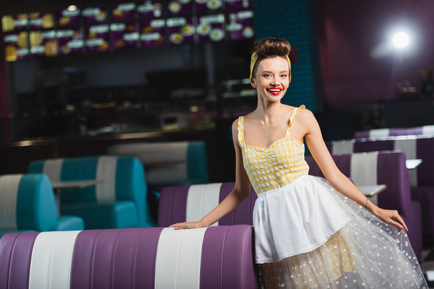positive pin up waitress in yellow dress standing in cafe  - Foto, Imagen