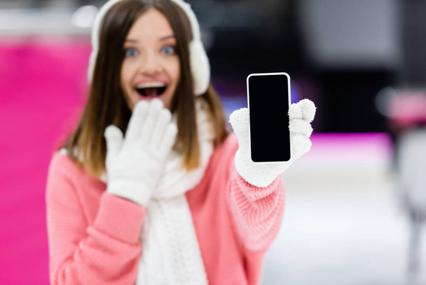 расплывчатая и изумленная женщина в перчатках держит смартфон с пустым экраном - Фото, изображение