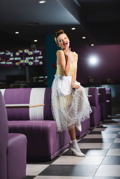 happy pin up waitress covering mouth in retro cafe  - Photo, Image