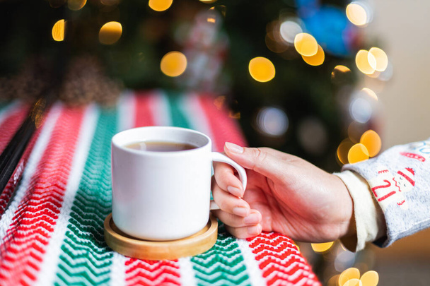 A closeup shot of a cup of hot chocolate near a Christmas tree - Fotografie, Obrázek