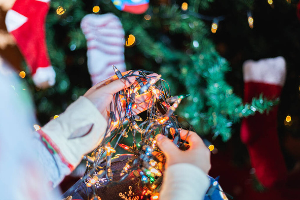 A closeup shot of a person in cozy pajamas holding illuminated Christmas lights - Zdjęcie, obraz