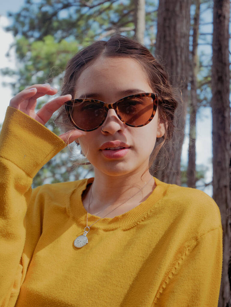 An attractive young girl wearing sunglasses and posing in a forest - Photo, image