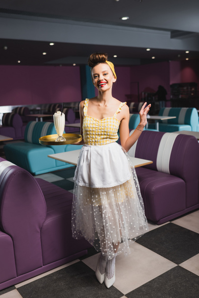 весела шпилька офіціантка тримає лоток з молочним коктейлем під час жестування в кафе
  - Фото, зображення