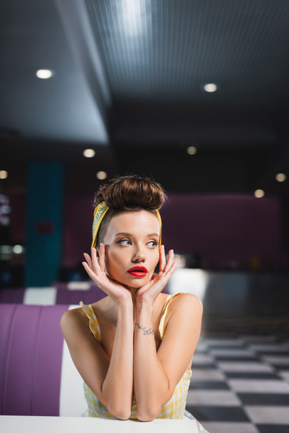 young pin up woman with tattoo looking away in cafe - Фото, изображение