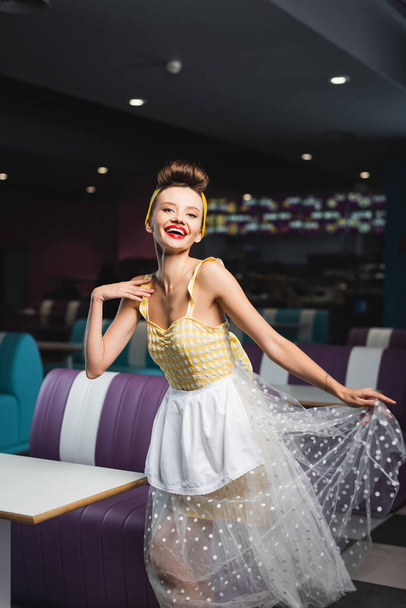 fröhliche Pin-up-Kellnerin im Kleid lächelt im Café - Foto, Bild