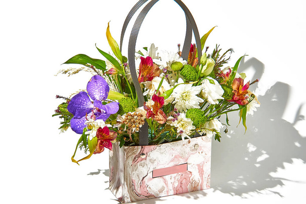 Arreglo floral en una bolsa de cartón con asas de plástico para arreglos florales sobre un fondo blanco con una sombra en el lado derecho. - Foto, imagen