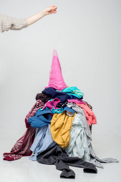 hand throws clothes into a pile with used clothes. Pile of used clothes on a light background. Second hand for recycling - Foto, imagen