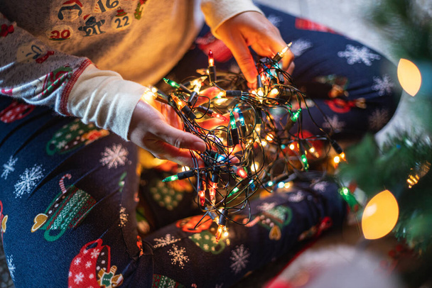 A closeup shot of a person in Christmas pajamas holding illuminated tree lights - Фото, зображення
