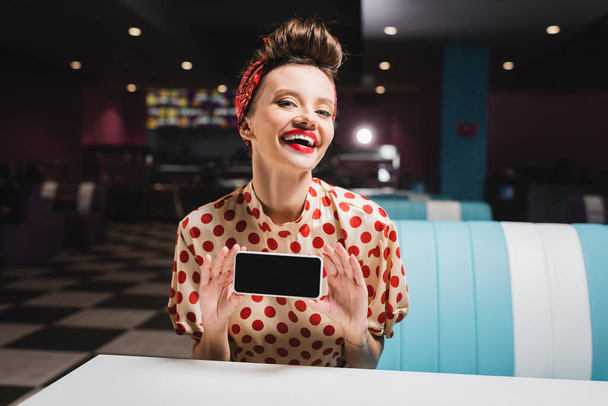 heureuse pin up femme avec lèvres rouges tenant smartphone avec écran vide  - Photo, image