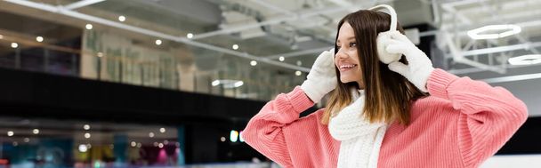 happy woman in pink sweater adjusting white ear muffs, banner - Foto, Imagem
