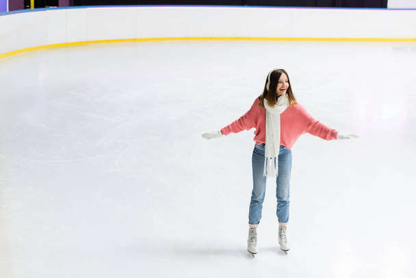 volledige lengte van verbaasd jonge vrouw schaatsen met uitgestrekte handen op de ijsbaan  - Foto, afbeelding