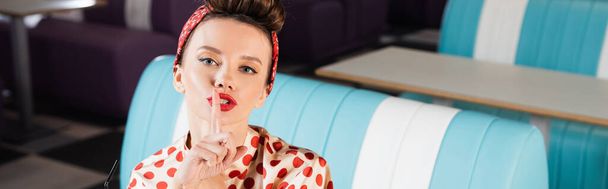 young pin up woman in red polka dot blouse showing hush sign in cafe, banner - Foto, afbeelding