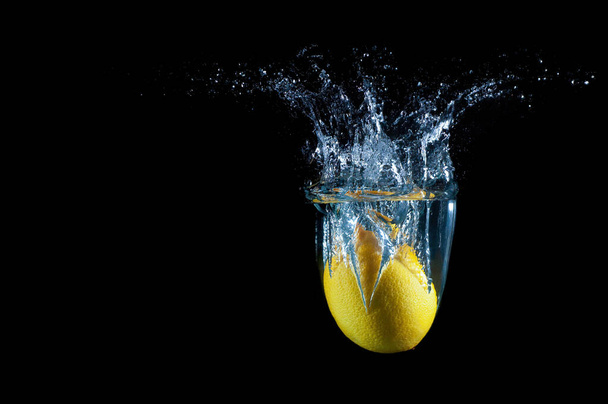 Lemon splashing in water against black background - Фото, изображение