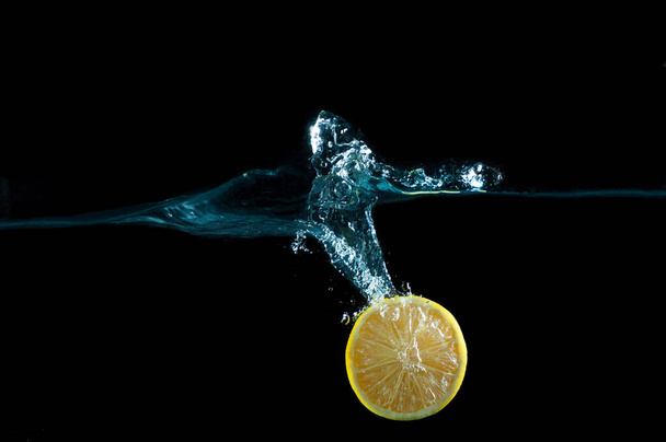 Half of a fresh lemon falling into water with splashes isolated on black background - Photo, image
