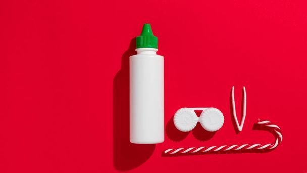 Contactlenzen, lenzen pincet en lensoplossing op een rode kerstachtergrond met suikerriet. Hoge kwaliteit foto - Foto, afbeelding
