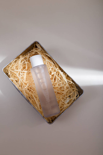 Mock up bottle of essence toner with no label in box with wood shavings filler in trendy natural solid light. Face skin care cosmetics, copy space - Photo, Image