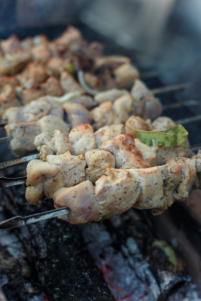 Soft focused shot of marinaded pork meat pieces on skewers frying over bonfire. Kebab or traditional shashlik cooking with lot of smoke. Vertical shot - Photo, Image