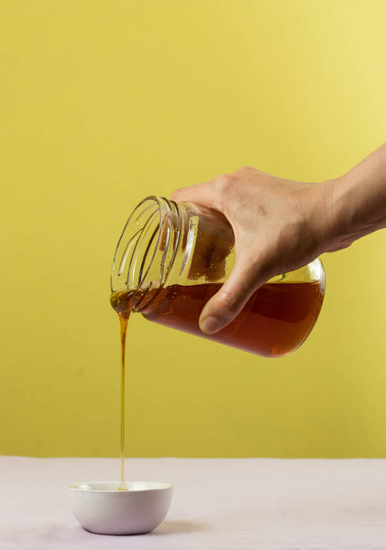 A hand pouring honey from a jar over a white bowl - Foto, Bild