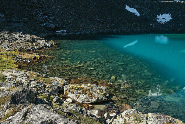Piękny krajobraz z turkusowym jeziorem górskim z przezroczystą wodą i kamienistym dnem. Jezioro lodowcowe Azure z przejrzystą powierzchnią wody w świetle słonecznym. Biały śnieg i zielony mech w pobliżu jeziora górskiego. - Zdjęcie, obraz