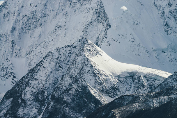 Φοβερό ορεινό τοπίο με μεγάλο βράχο χιόνι με κορυφώθηκε κορυφή στο παρασκήνιο του γιγαντιαίου καλυμμένο με χιόνι βουνό τοίχο στον ήλιο. Ατμοσφαιρικό τοπίο με χιονισμένα βουνά στο φως του ήλιου. Μεγάλα χιονισμένα βουνά - Φωτογραφία, εικόνα