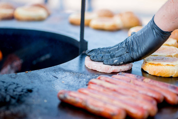 cook hands in gloves grill burger buns and sausages - Photo, Image