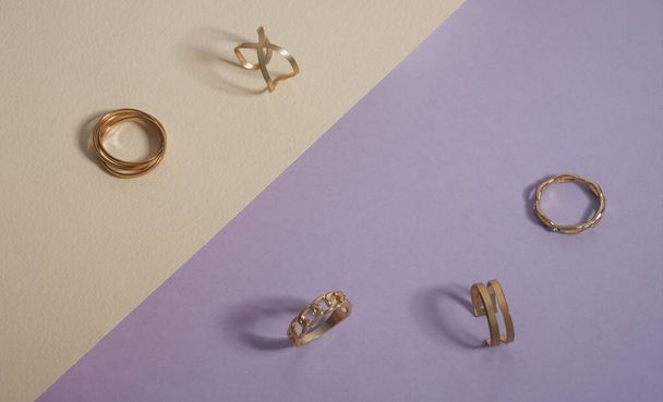Vista superior de la colección de anillos dorados sobre fondo púrpura y beige - Foto, imagen