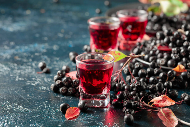 Black chokeberry liquor and fresh berries on a dark blue background. - Фото, изображение