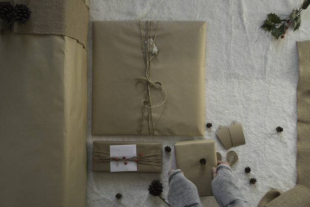 Geri dönüştürülmüş kahverengi ambalaj kağıdı hediye paketi. Bir insanın elleri hediyeyi indiriyor.. - Fotoğraf, Görsel