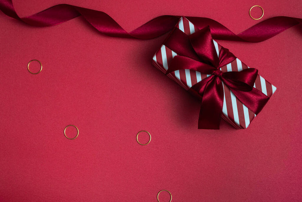 Caja de regalo a rayas con un lazo rojo sobre un fondo de color. Primer plano monocromo. - Foto, imagen