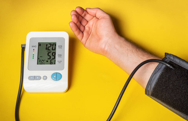 A pessoa mede sua própria pressão arterial na mesa médica amarela. Cuidar da sua própria saúde. Máquina de pressão arterial digital mostra um bom resul - Foto, Imagem