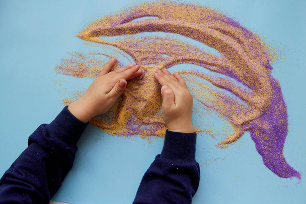 子供の手はカラフルな砂で遊ぶ。子供の細かい運動能力の開発。創造的な子供の職業。上からの眺め - 写真・画像