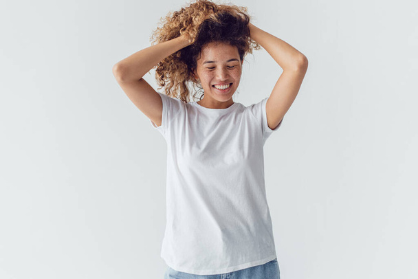Smiling woman with lush curly hair in white blank t-shirt on a white background. Mock-up. - Foto, immagini