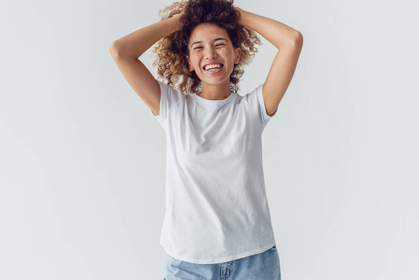 Smiling woman with lush curly hair in white blank t-shirt on a white background. Mock-up. - Fotoğraf, Görsel
