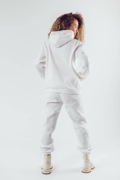 Woman with thick curly hair in a white suit from a hoodie and sweatpants back view. - Foto, Imagem