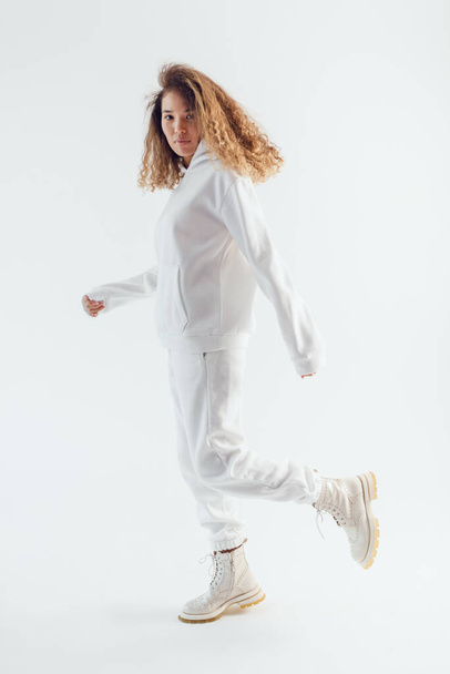Attractive woman with thick curly hair in a white suit of hoodies and sweatpants. Mock-up. - Zdjęcie, obraz