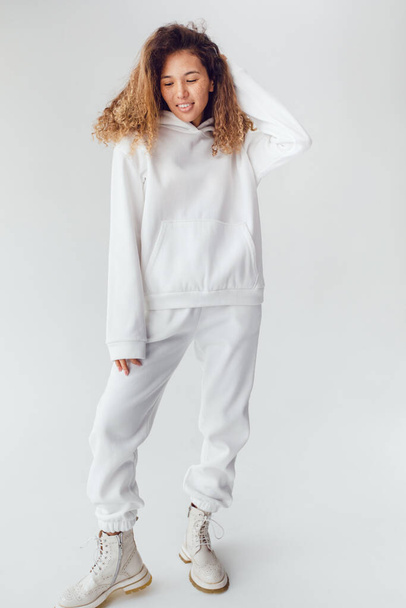 Attractive woman with thick curly hair in a white suit of hoodies and sweatpants. Mock-up. - Foto, immagini